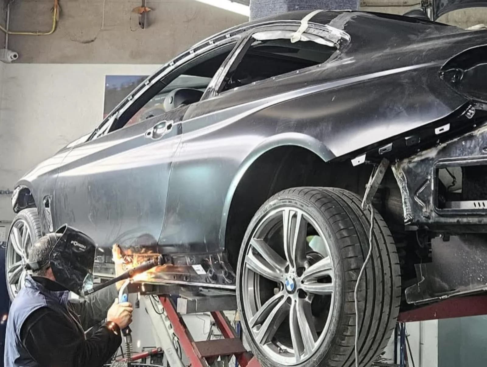 Carrossier au masque de soudure intervenant sur le bas de caisse d'une BMW levée sur pont, avant déposé